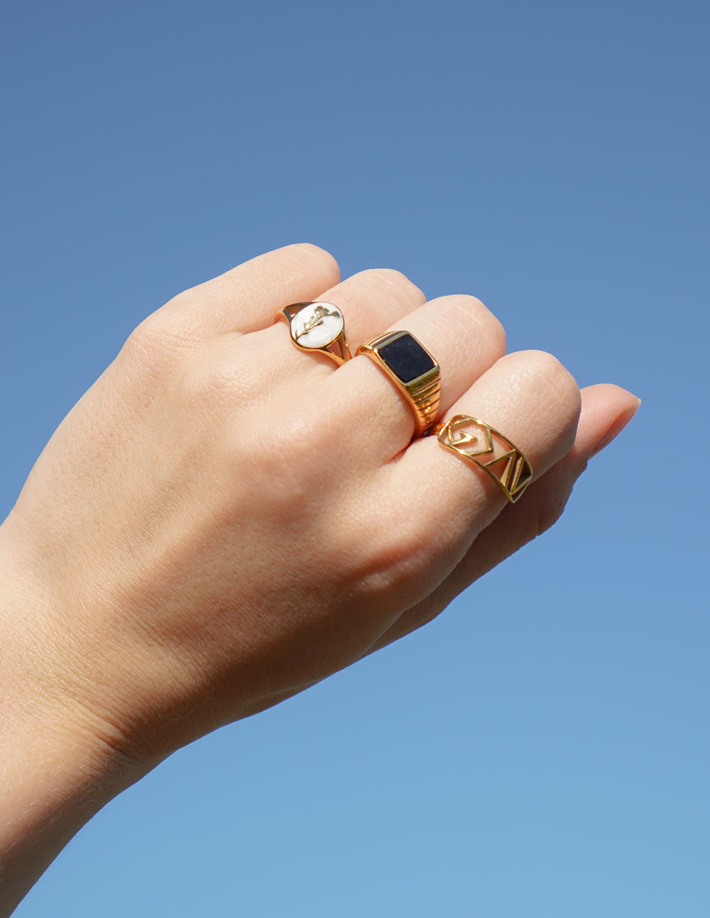 Hand wearing three gold rings against a clear blue sky