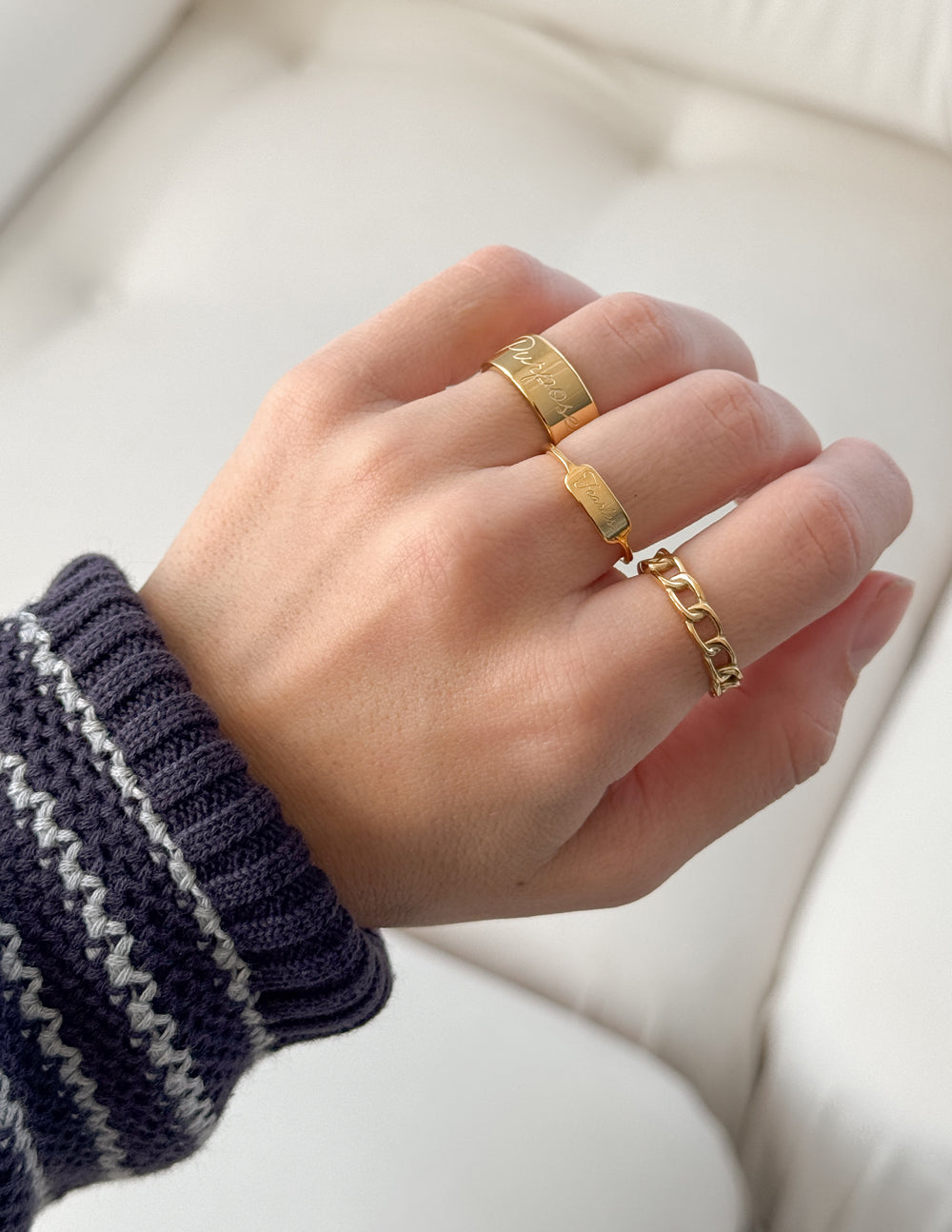 Hand wearing two gold rings on a neutral background