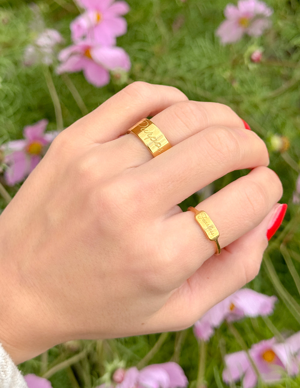 Hand wearing two gold rings with engraved text against a floral background
