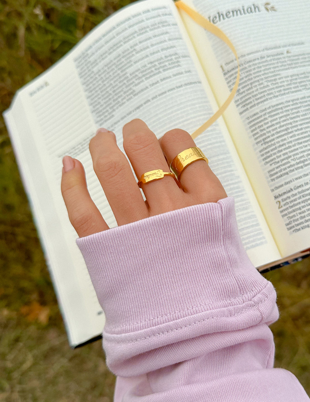 Hand wearing a gold ring with an open book in the background