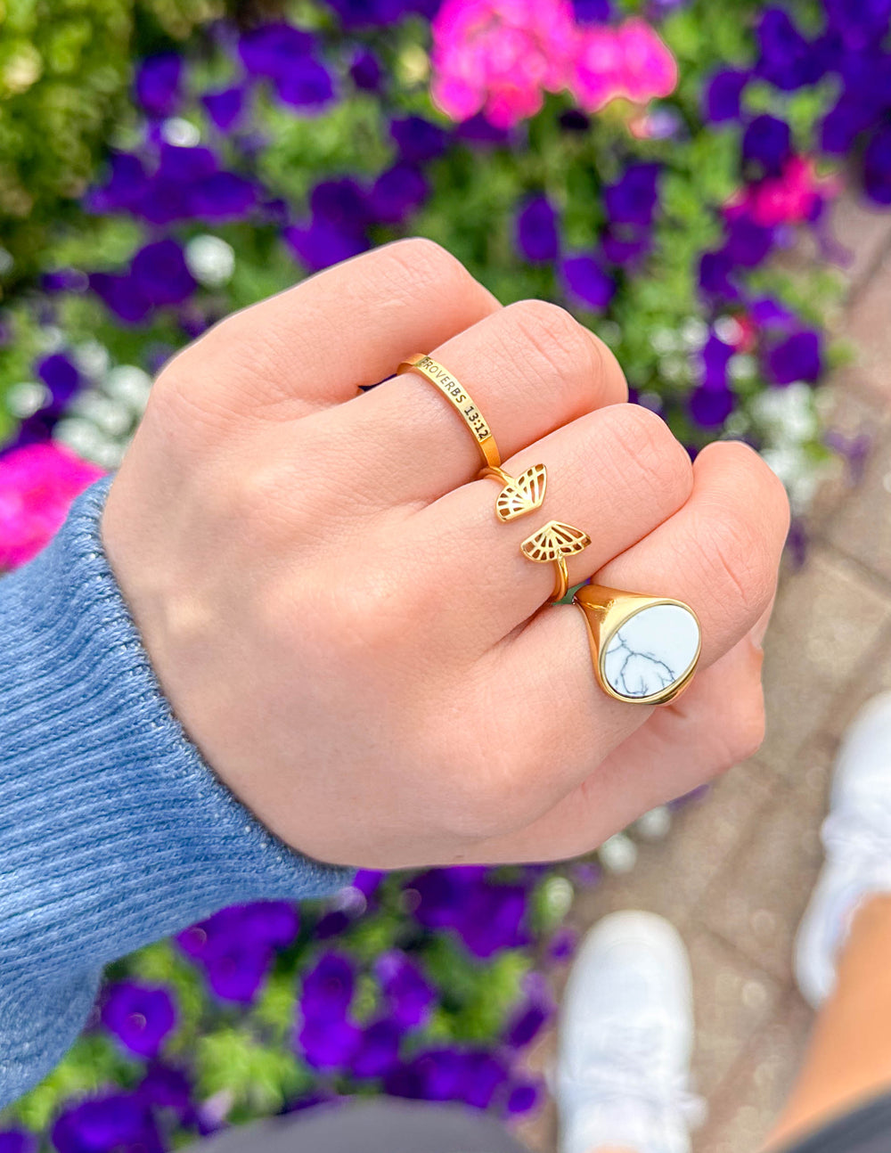 Hand wearing gold rings with a blurred floral background