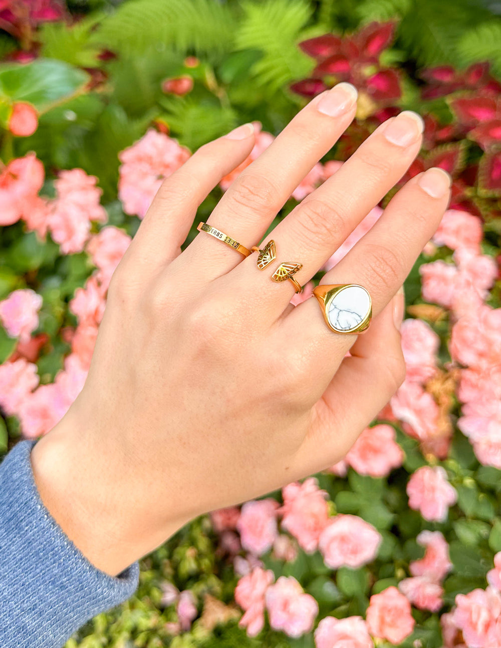Hand wearing gold rings with a floral background