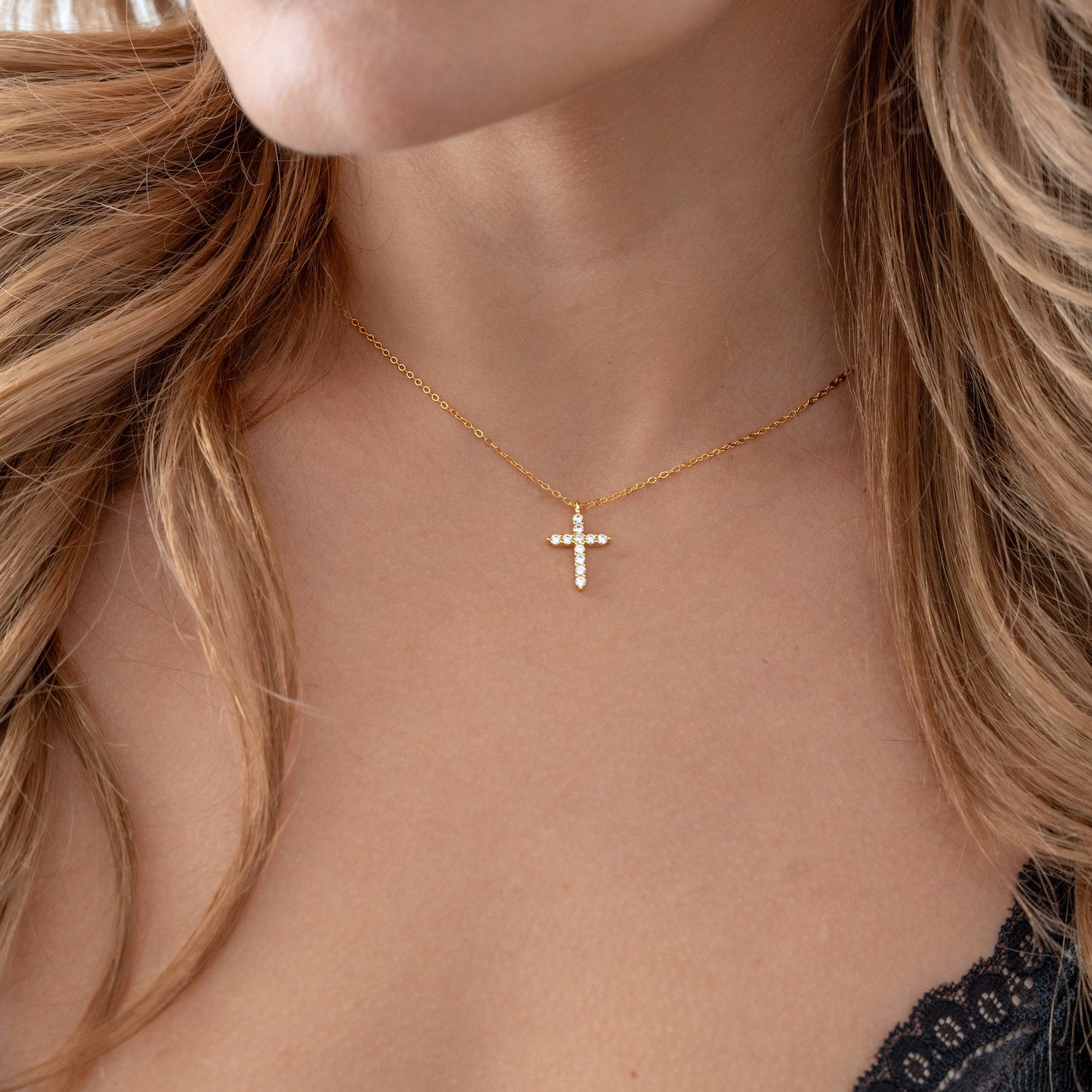 Gold necklace with a cross pendant on a person with blonde hair.