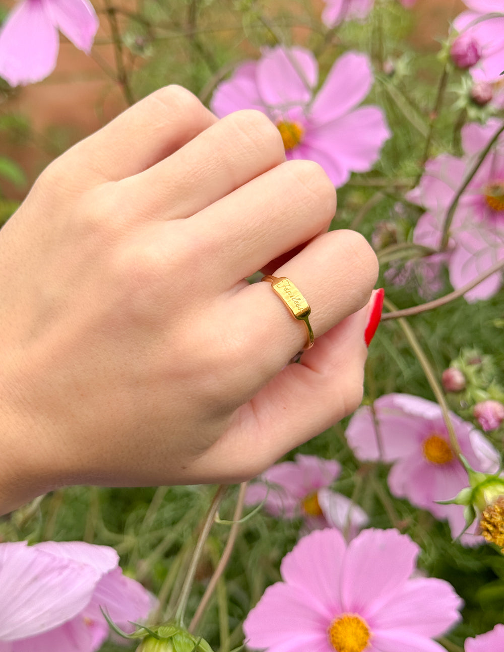 Hand wearing a gold ring with pink flowers in the background