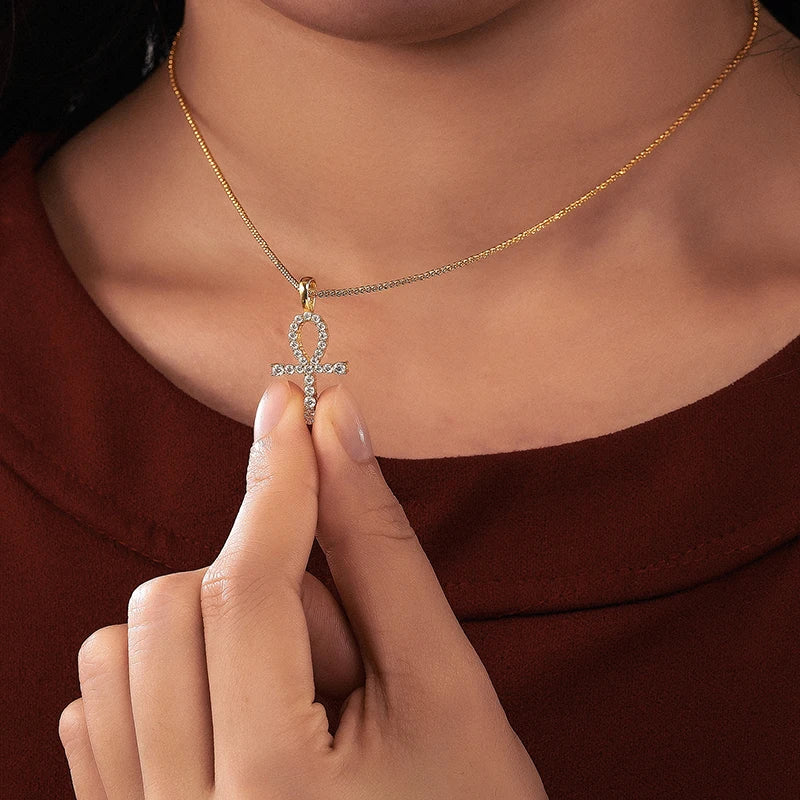 Necklace with an ankh pendant held by a hand against a brown background