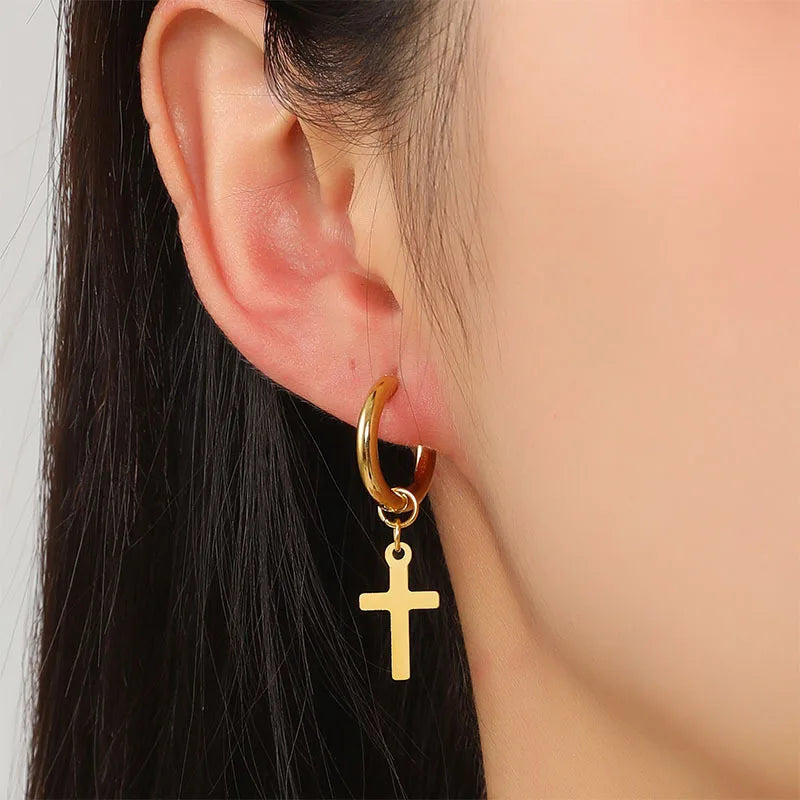 Gold hoop earring with a cross pendant worn by a person.