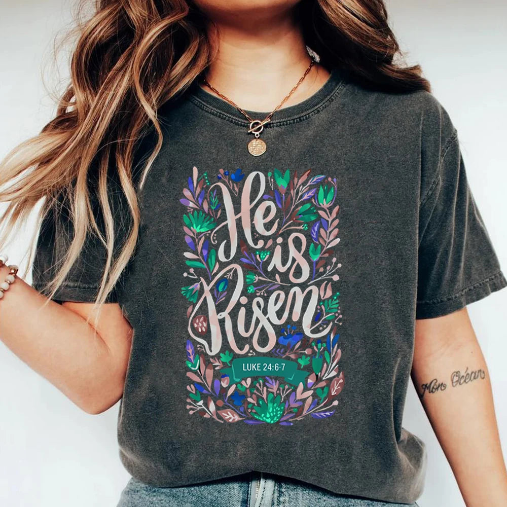 Person wearing a dark gray t-shirt with 'He is Risen' design and Bible verse.