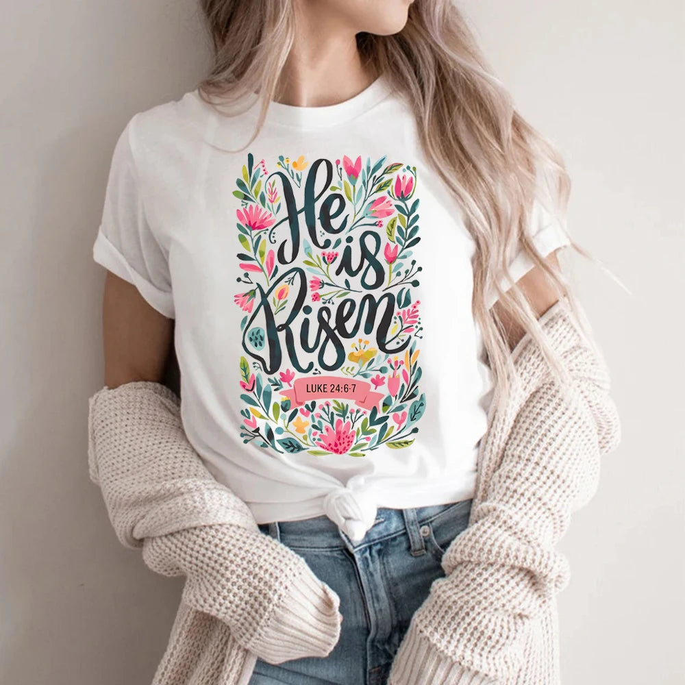 Person wearing a white t-shirt with 'He is Risen' design and floral elements.