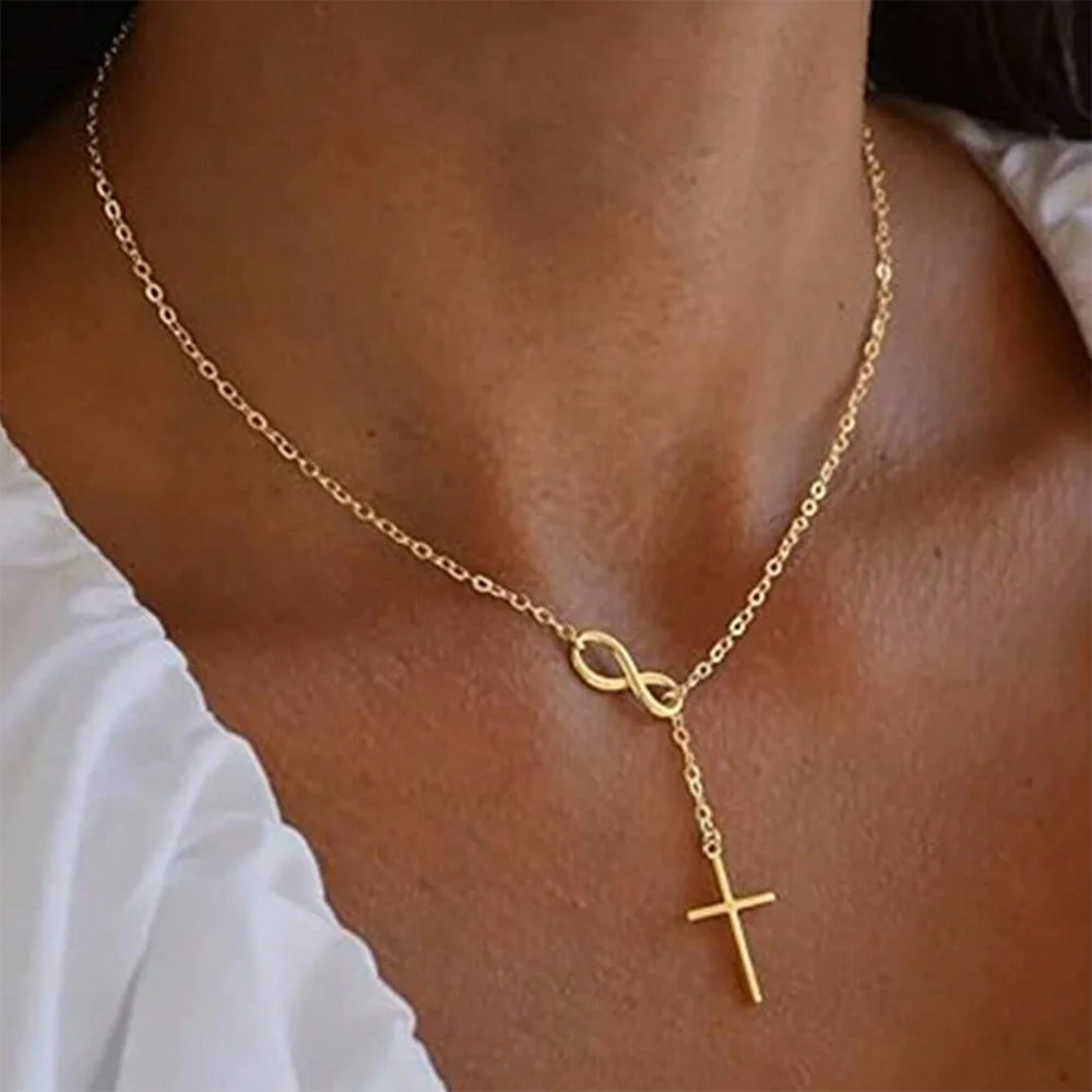Gold necklace with infinity and cross pendants on a person wearing a white shirt.