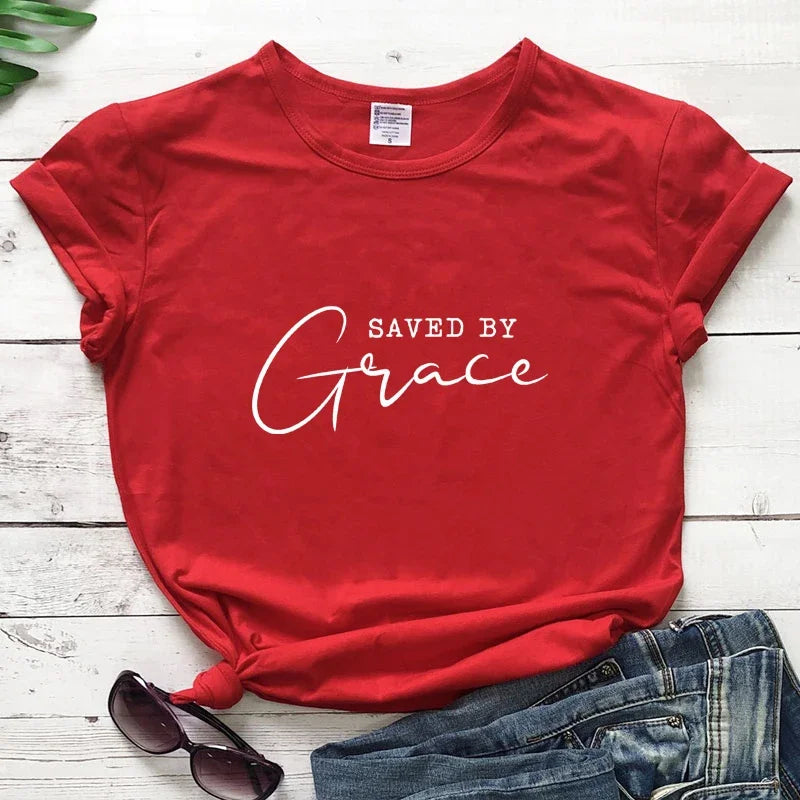 Red t-shirt with 'Saved by Grace' text on a wooden surface with jeans and a lime.