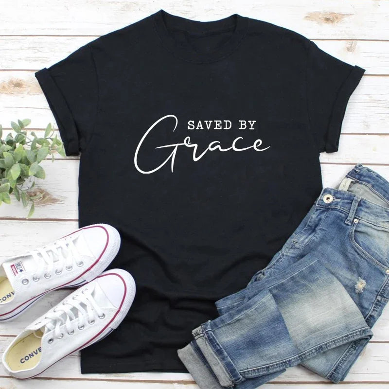 Black t-shirt with 'Saved by Grace' text on a wooden surface with jeans and a lime.