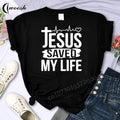 Black t-shirt with 'Jesus Saved My Life' text on a white background with shoes and jeans.