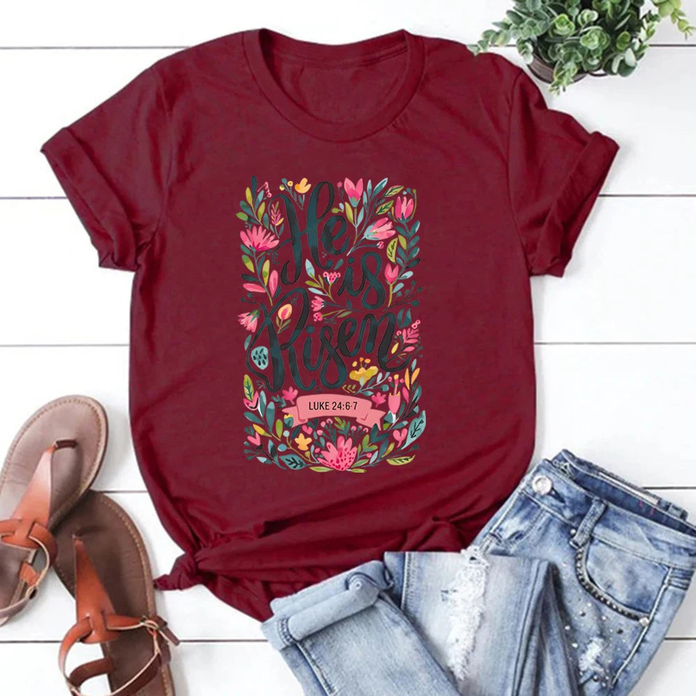 Red t-shirt with floral text design on a white wooden surface with sandals and jeans.