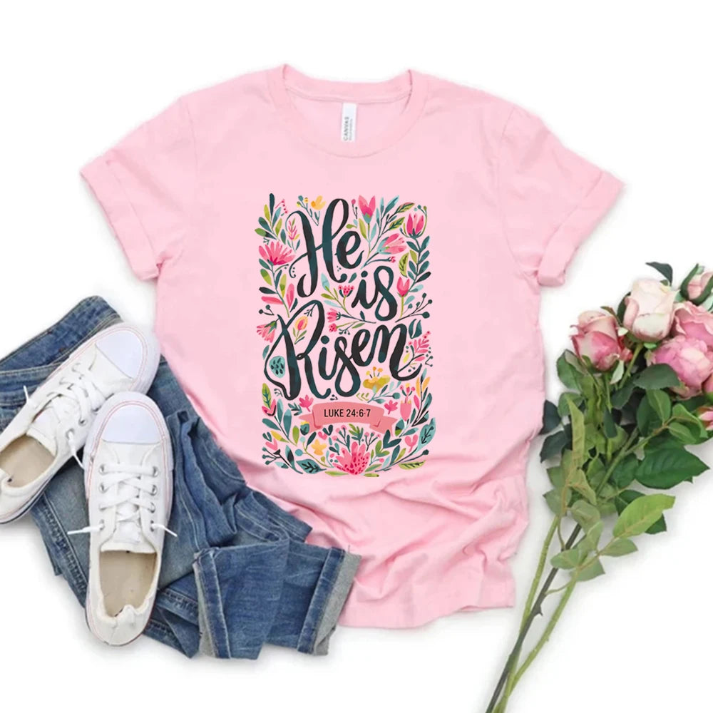 Pink t-shirt with 'He is Risen' design, paired with jeans and sneakers on a white background.