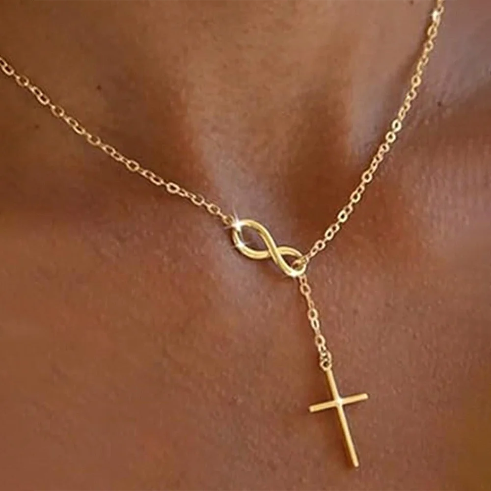 Gold necklace with infinity and cross pendants on a person's neck.