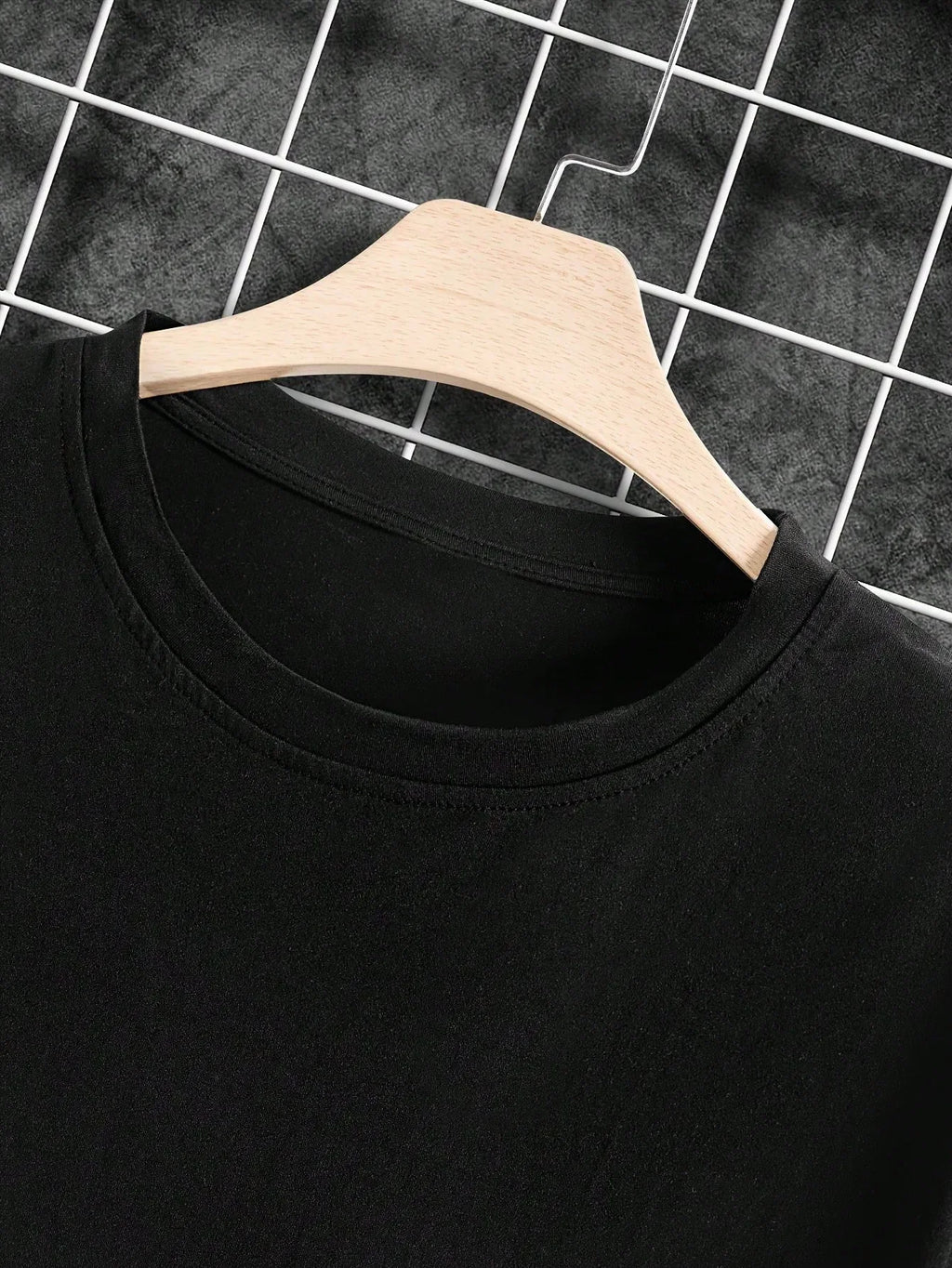 Black t-shirt on a wooden hanger against a grid background